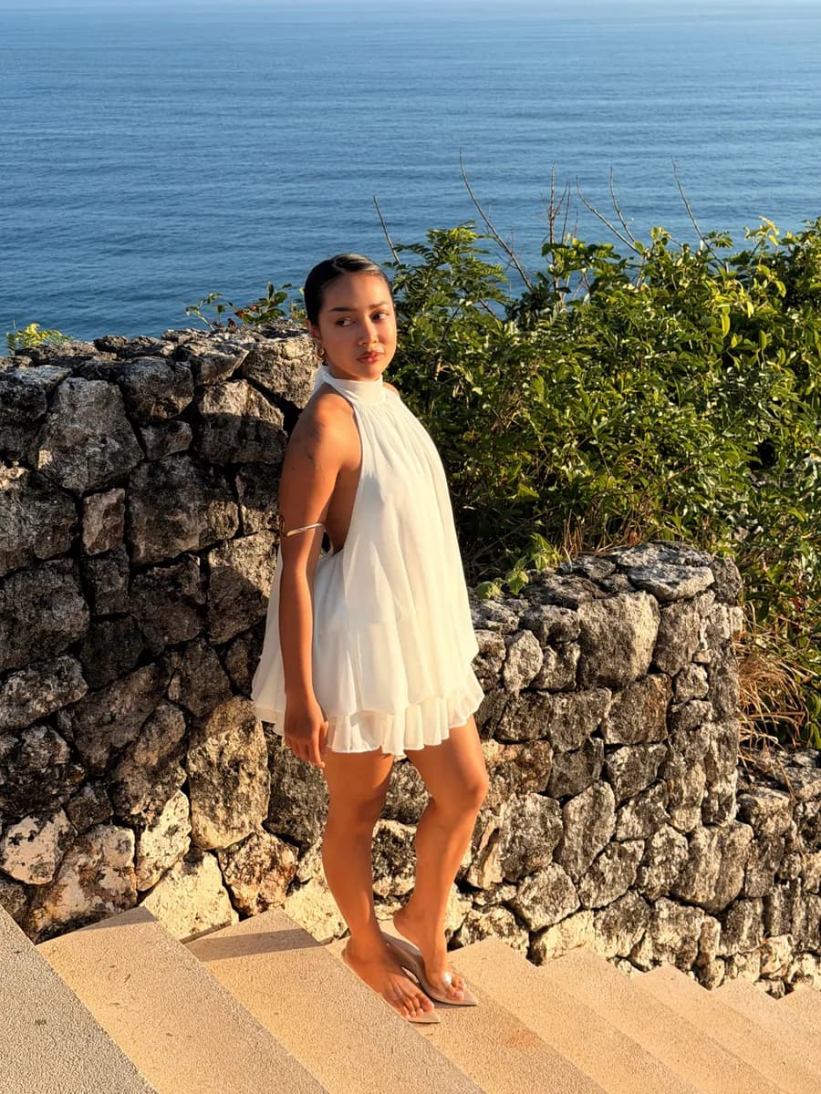 Jean in a white halter dress on stone steps above the ocean at sunset